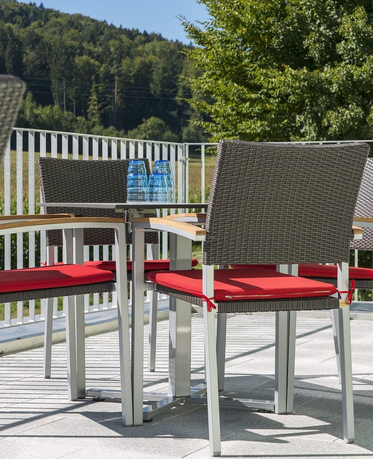 Nahaufnahme von Sitzmöglichkeiten auf einer sonnigen Terrasse mit Blick ins Grüne