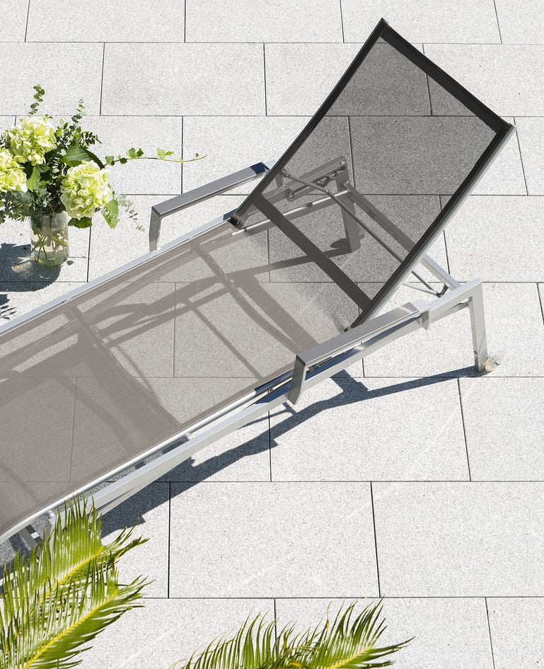 Aufsicht auf einen grauen Liegestuhl auf einer sonnigen Terrasse