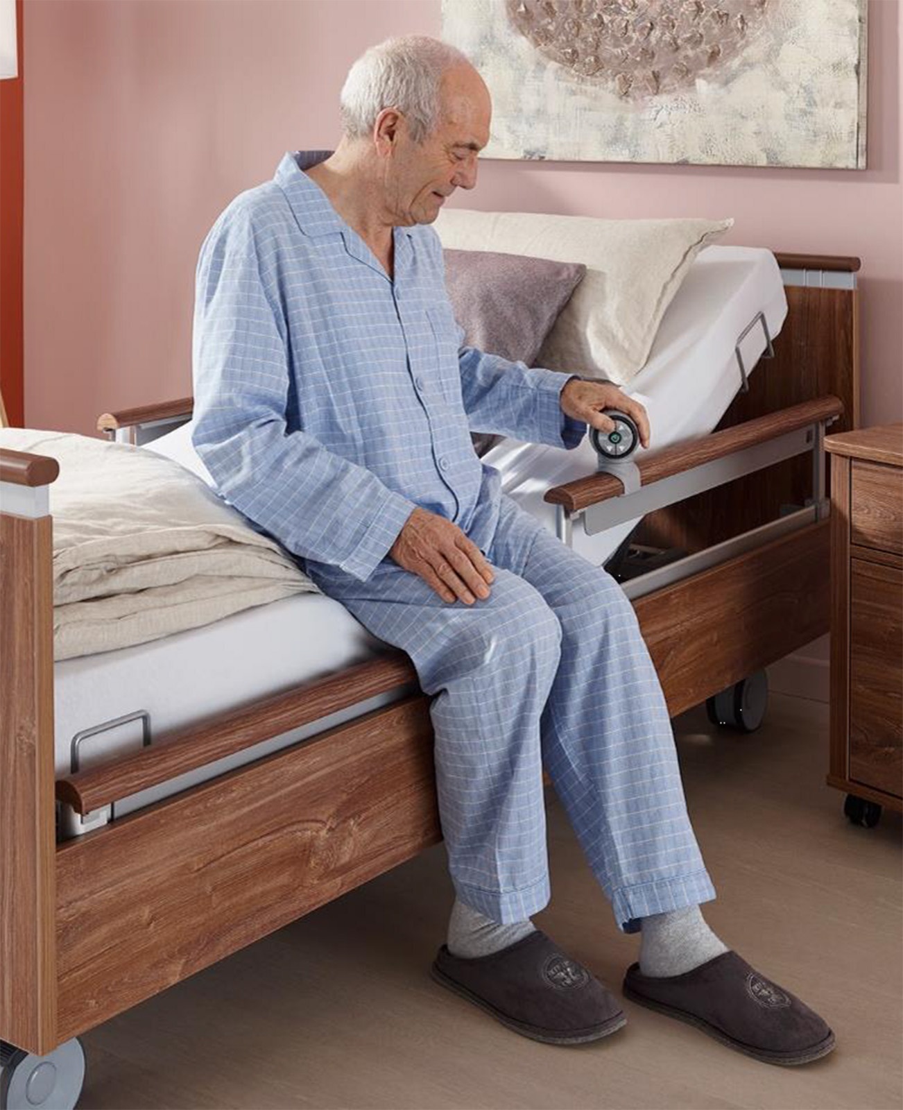 Mann hockt auf der Bettkante des Niedrigpflegebetts und bedient den SafeLift-Controller