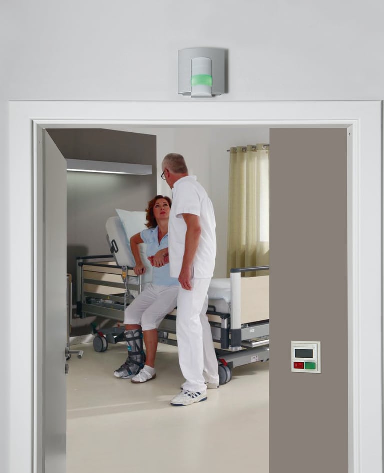Ein Betreuer steht bei der Patientin, die durch ihr Aufstehen das Rufsystem aktiviert hat, am Bett und betreut sie