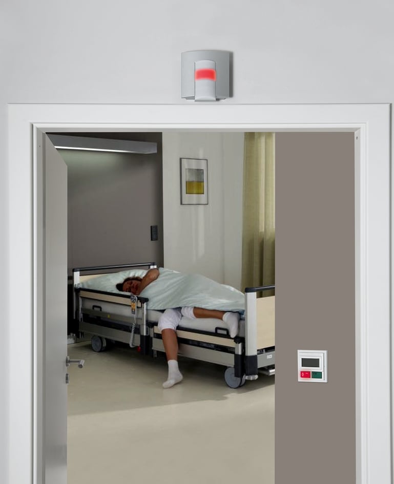 Patientin steht aus einem Spitalbett auf und an der Zimmertür leuchtet ein rotes Nachtlicht auf, das das Rufsystem aktiviert
